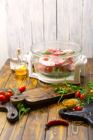 Electric convection oven on a wooden table. Cooking meat on an air grill. Fresh meat, wine and vegetables. Selective focus, place for text.の写真素材
