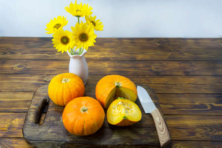 Pumpkins on dark wooden table and knife. Beautiful yellow flowers in vase. Autumn still life. Concept of eco products, autumn harvest of vegetables. Selective focus.の写真素材