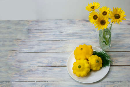Still life on a wooden table in the fall. Yellow flowers in a glass vase and round yellow zucchini...
