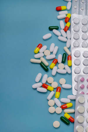 Tablets in blisters and scattered capsules of various medicines on blue background. Antibiotics and aspirin for health. Medicine and pharmacy concept.の写真素材