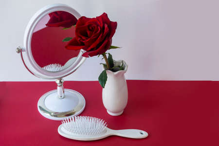 Hairbrush, mirror and red rose in white vase on the table. Hair care concept, healthy hair, beauty....