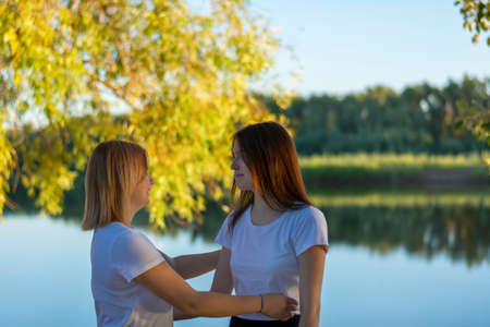 Two girls friends hold each other's hands for a walk near the river. Cropped view, rear view, selective focus. The concept of friendship, relationships.の写真素材