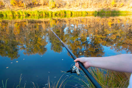 Young woman fisherman catches fish with fishing rod in autumn on the river. Fisherman's day concept.の写真素材