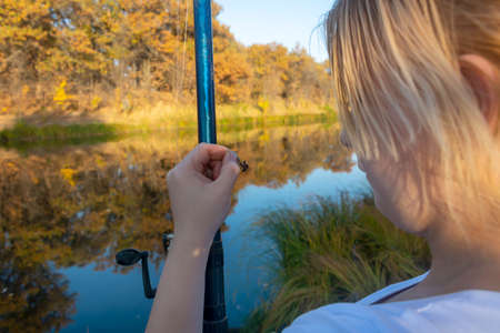 Young woman fisherman catches fish with fishing rod in autumn on the river. Fisherman's day concept.の写真素材