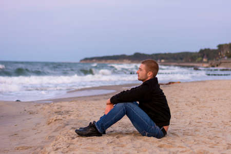 Smiling young Caucasian man with beard on background of the sea and waves with white foam. Selective...