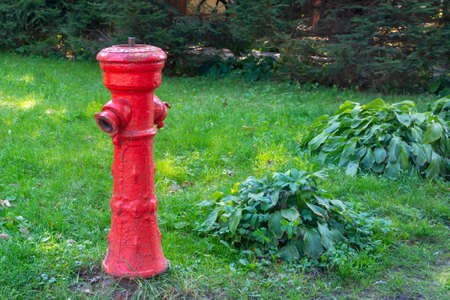 Old fire hydrant of red color on the green grass of the lawn. Fire safety concept. Selective focus,...