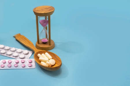 Tablets in a wooden spoon on a blue background. Hourglass and blisters with pills, time to take...