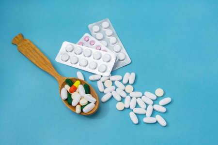 Pills and capsules of medicines in large spoon on blue background. Close-up, selective focus.