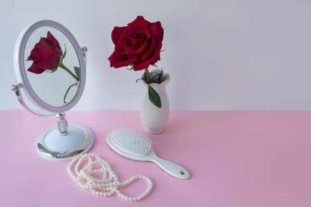 Red rose in white vase on table with hairbrush and pearls. Wedding preparation concept. Selective...