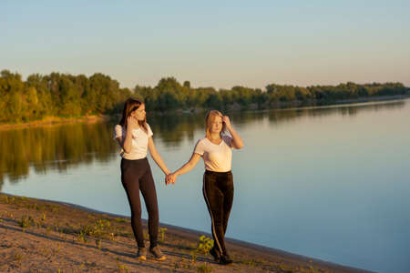 Two friends hold hands and walk along the river bank. Friendship and love concept. Soft focus, blur.の写真素材