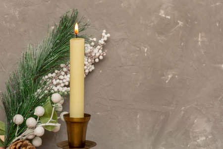 Fire of white candle against background of Christmas tree branch and gray concrete wall. Selective focus, blurred background, copy space.の写真素材