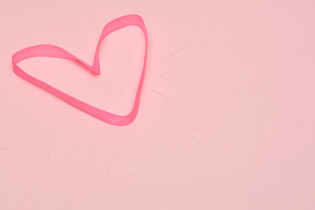 Heart of silk ribbon on pink textured background with copy space. Concept for Valentine's Day, love, wedding.の写真素材