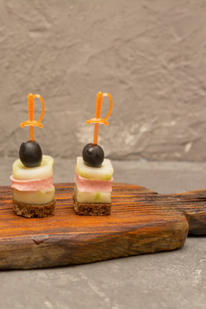 Canapes on skewers with dark bread, ham and olives. Buffet table, selective focus.