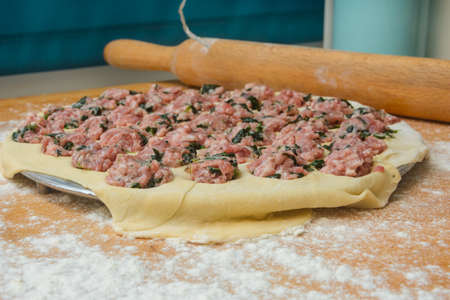 Cooking dumplings in iron round form. Minced meat with spinach on thin crust. Close-up, selective focus, blur.の写真素材