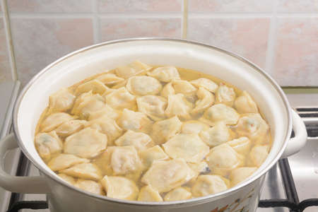 Homemade dumplings in saucepan with hot broth and spices. Close-up, selective focus.