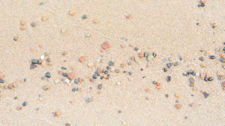 Small pebble stones on wet sandy seashore. Wide format, panoramic landscape. Selective focus, copy space.の写真素材