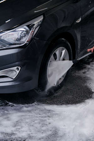 Detergent is washed with water from the front wheel of a gray car at the sink