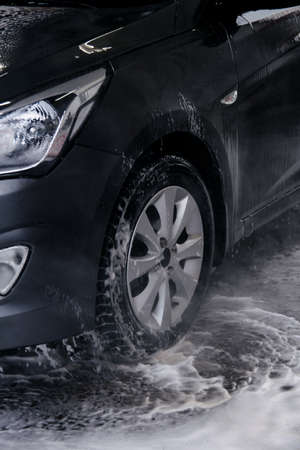 Using a car wash, wash off detergent from a gray car with water