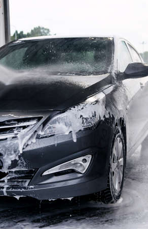 Detergent is washed off the front of a gray car with waterの写真素材