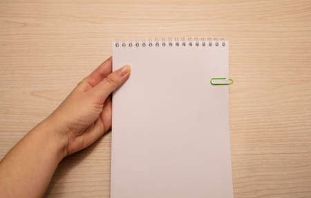 Left female hand holds a white notebook on a wooden background