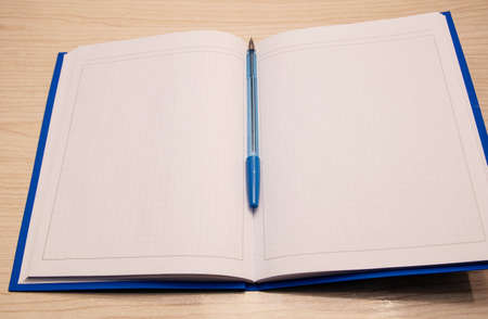 White blank notepad to the writing cage lies on a wooden background with a blue pen