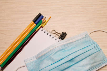 Painting brushes, pencil, pens, paper clip, disposable medical mask and white blank notebook on a...
