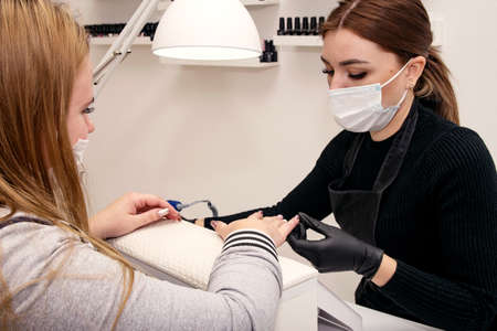Young girl manicurist at the work table holds the hands of the clientの写真素材