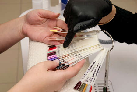 Palette with nail polishes in the hands of the master and the client