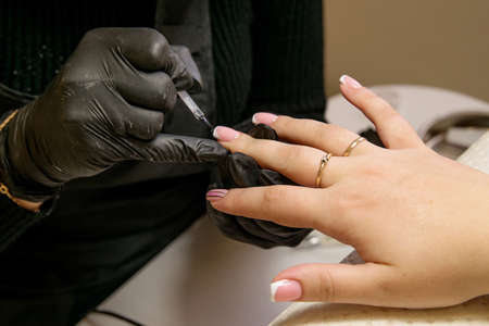 Close-up shot of a manicurist in black gloves applying gel polish on nails