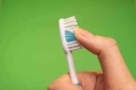 Blue Toothbrush in woman's right hand against a green background with fingers guided through the bristlesの写真素材