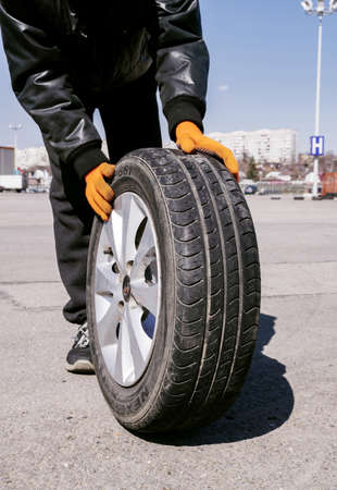 April 10, 2021 Russia. Tula. Parking lot at the shopping center Maxi. Man wearing orange gloves rolls black wheelのeditorial素材