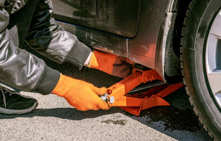 Car mechanic man wearing gloves lifts small orange car jack