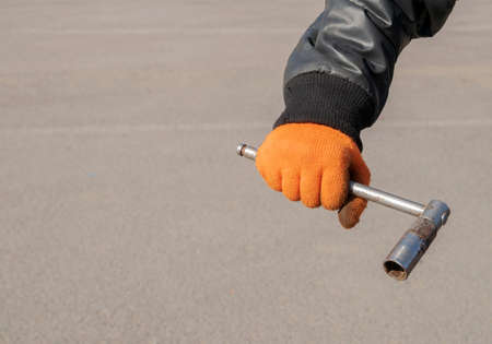 Metal wheel wrench in the hands of a man wearing orange gloves and a black twist