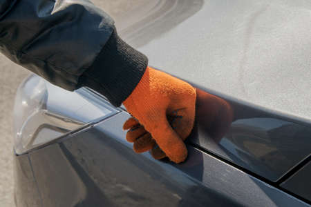 Worker in orange gloves has his hand on the hood of a gray autoの写真素材