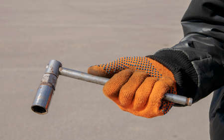 Metal wheel wrench in the hands of a man wearing orange gloves and a black twistの写真素材