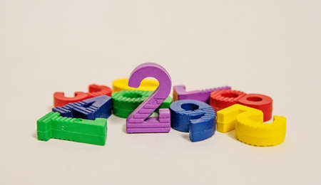 Multicolored small bright children's numbers for development from zero to nine lie randomly on a white background and the number two standsの写真素材