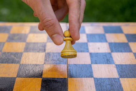 Male hand holding one chess piece of white pawn over empty chessboard