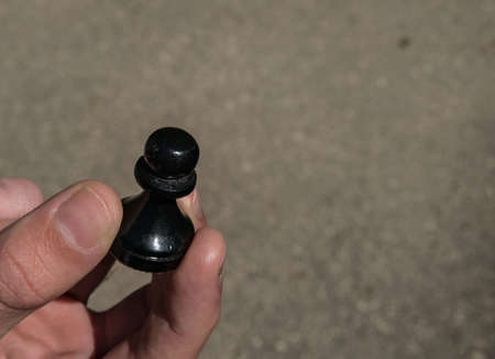 Male right hand holding one black pawn chess piece on solid backgroundの写真素材