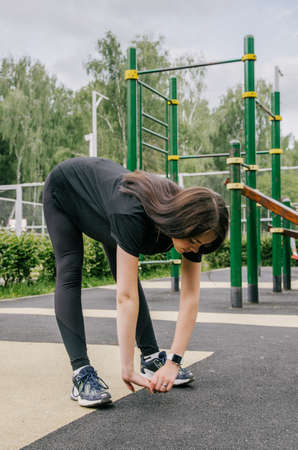 a girl in a black T-shirt and leggings performs a sports exercise stretching arms to legs
