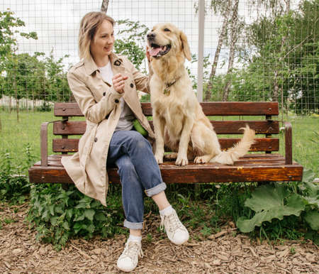 The mistress girl sits on a bench with her dog of the Golden Retriever breed and hugs
