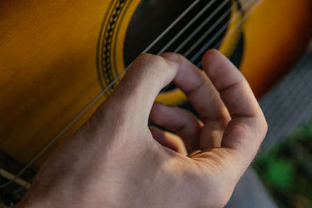 A man, whose face is not visible, plays the guitar on a musical instrument, sitting in natureの写真素材