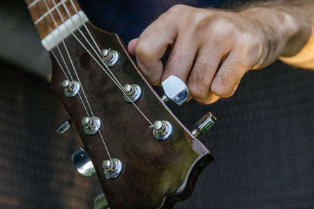 close-up of a male hand twisting the tuning pegs on a guitar neck