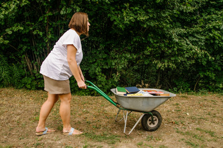 08/01/2021 Russia, Tula, a girl carries a garden wheelbarrow filled with old books on the groundの写真素材