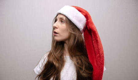 Portrait of a young brunette girl in santa claus santa hat in profile looking to the side