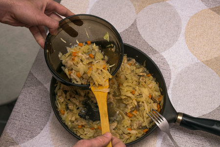 A portion of cooked stewed cabbage with pork is placed on a plate with a wooden spatula in a man's handの写真素材