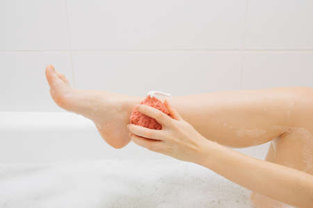 The girl in the bathroom in the foam rubs her legs with a washclothの写真素材