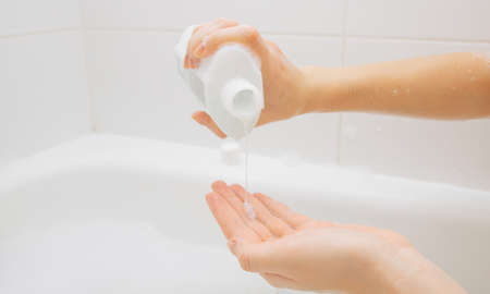 A girl in a white bathroom pours a product from a can of shampoo into her hand