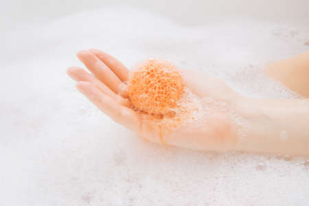 A girl in a white bathroom with foam dissolves a bright bath bomb in waterの写真素材
