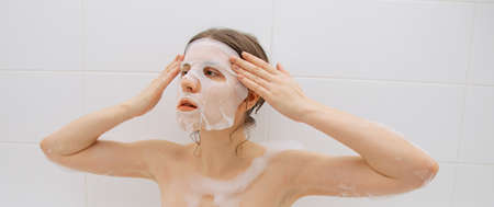Girl in a white bathroom with foam makes a moisturizing sheet mask for the face
