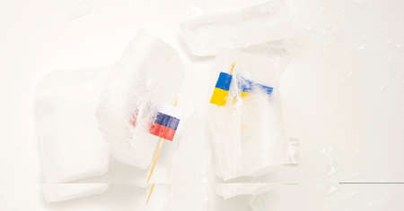 The split of two friendly countries. Two flags frozen in ice flags of Russia and Ukraine on a white...